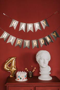 Artistic birthday setup with a cake, number balloon, and classic sculpture against a red wall.