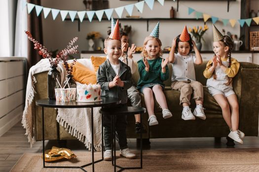Group of children celebrating a birthday with cake and party hats indoors.