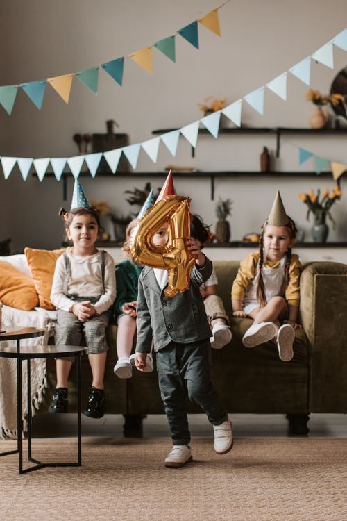 Free Group of kids celebrating a 4th birthday with balloons and party hats indoors. Stock Photo
