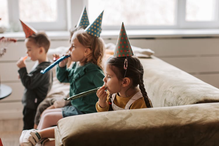 Children Sitting On Sofa Wearing Party Hats