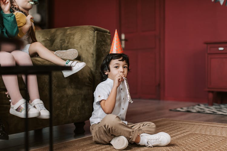 Boy Sitting On The Floor Blowing A Party Horn