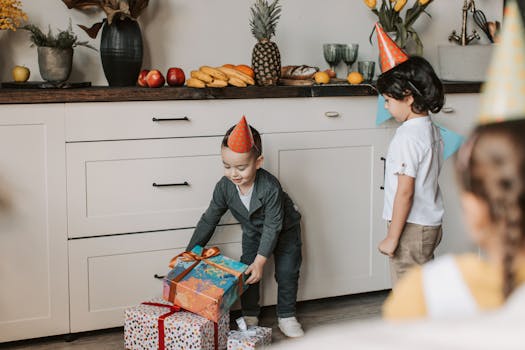 Young children enjoying a birthday celebration with gifts and party hats indoors.