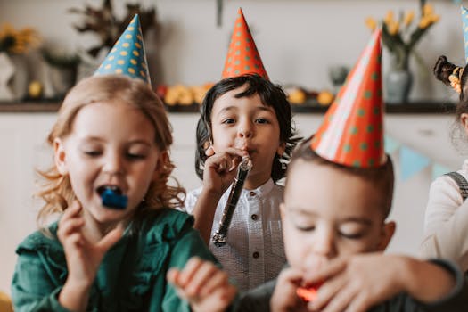 Group of children having fun at a birthday party with party hats and party horns indoors.
