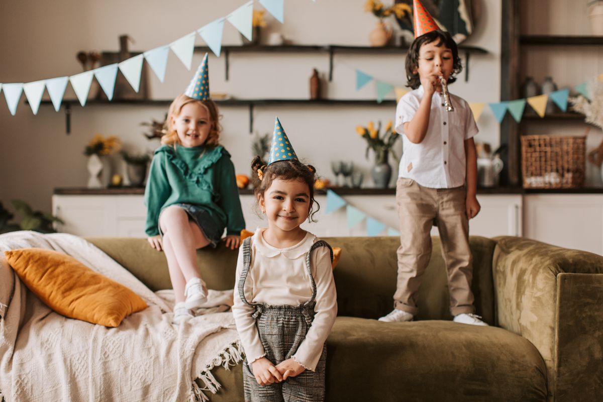 Three children in party hats celebrating a birthday with decorations