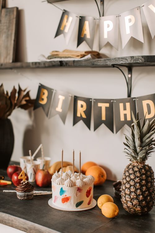 Free A festive birthday setup with cake, fruits, and decoration banners indoors. Stock Photo