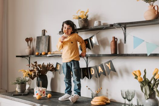 A joyful child in a yellow sweater enjoys a birthday treat indoors.