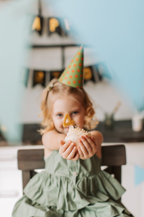 Free Little Girl with a Birthday Hat Holding a Cupcake with a Candle in a Shape of Number 4 Stock Photo