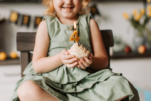 Happy child holding a cupcake with number four candle, celebrating a birthday indoors.