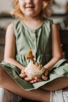 A child in a green dress holds a birthday cupcake with a "4" candle.