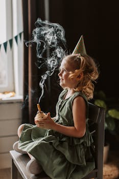 Adorable girl in party hat with cupcake lit, enjoying her birthday indoors.