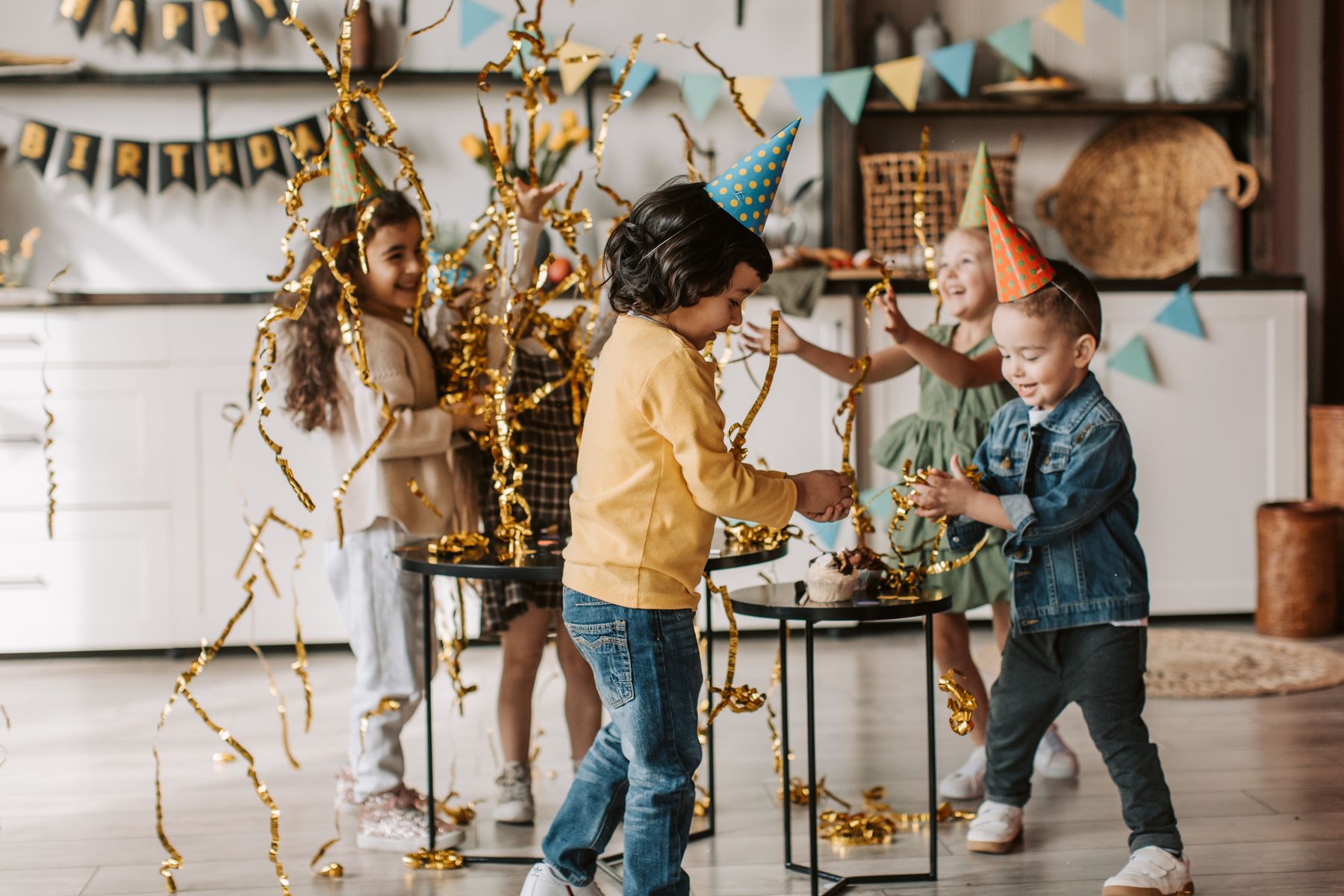 Kids playing with party streamers in a bright decorated birthday room.