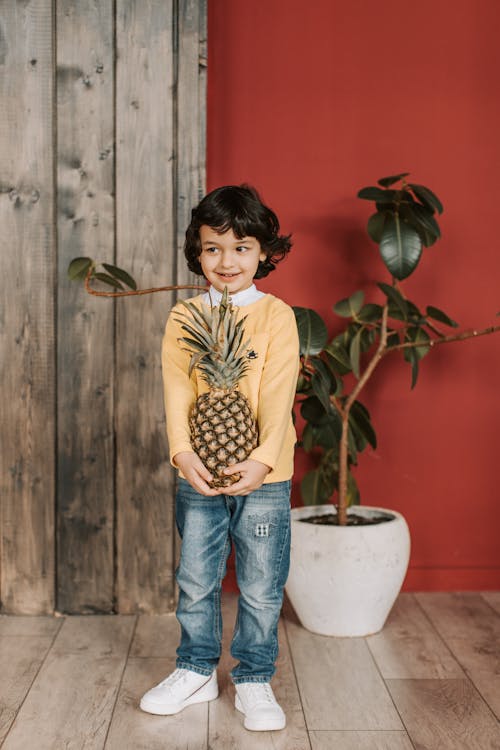 Boy in Yellow Long Sleeve Shirt Holding Pineapple