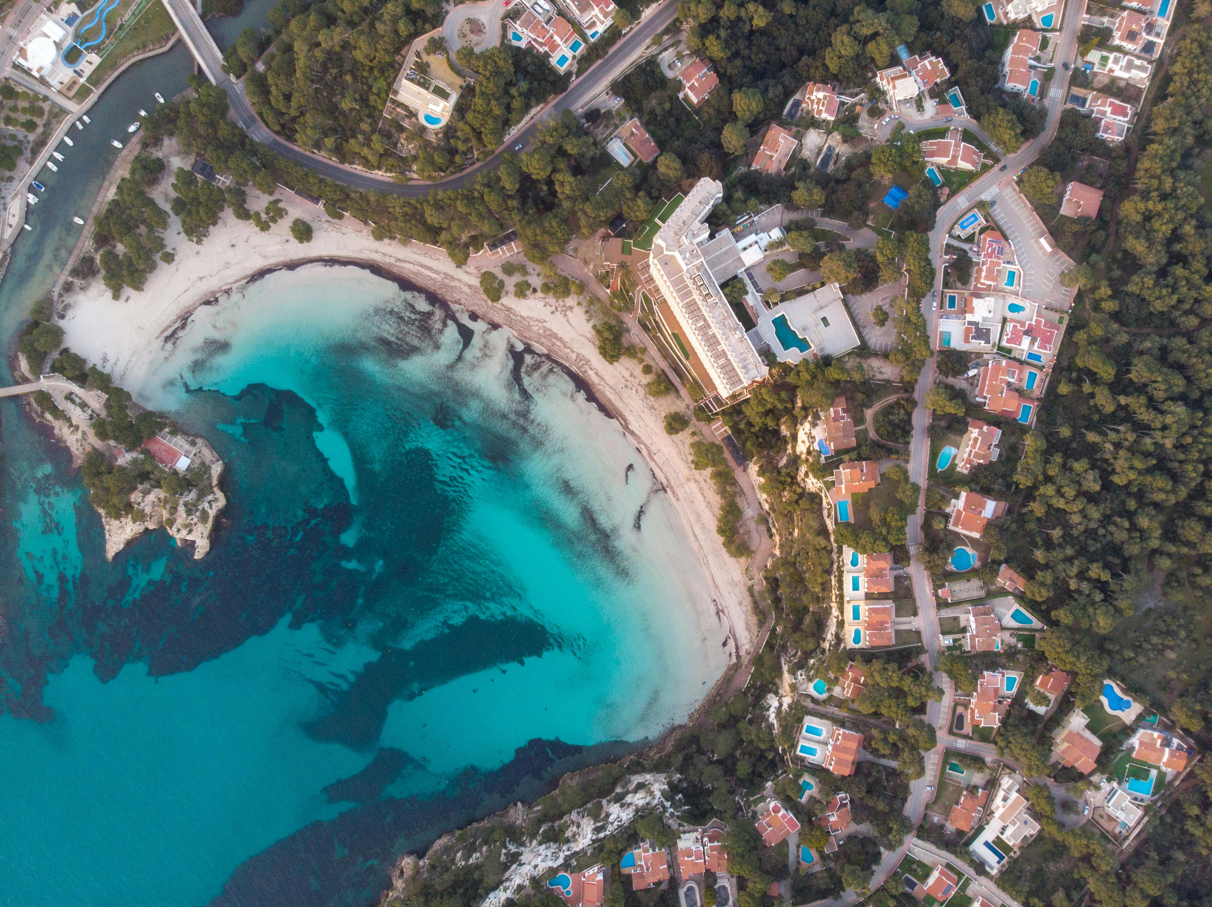 Explore the breathtaking aerial view of Ciudadela de Menorca's turquoise waters and luxury villas along the coast.