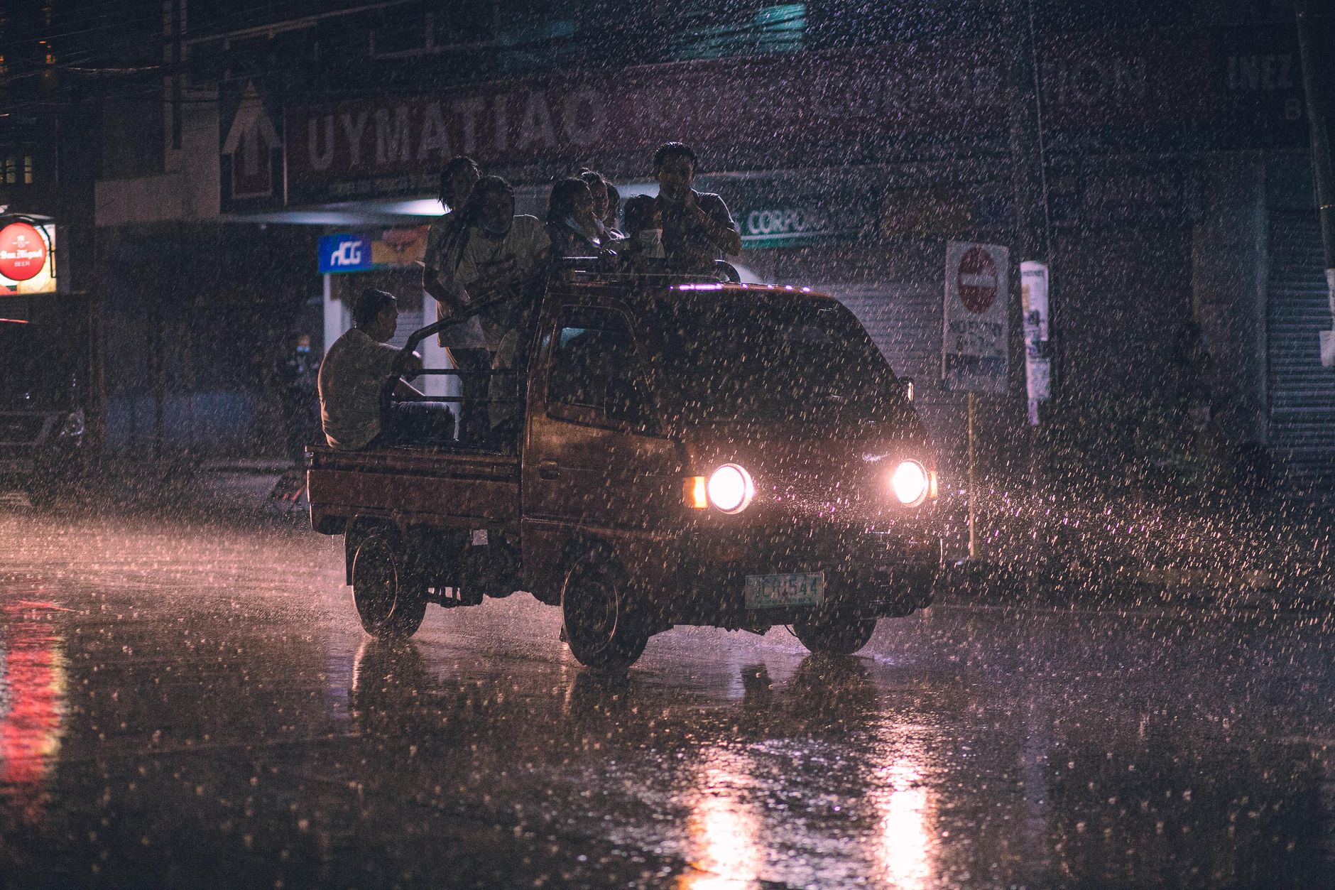 A group of people ride in a truck at night during heavy rain, headlights glowing in the dark.