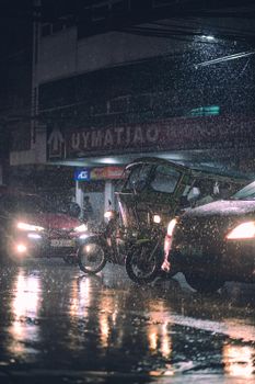 A city street scene at night with cars and a motorbike under rain, captured in wet conditions.