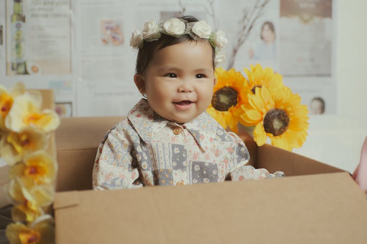 Happy Ethnic Child With Flower Wreath In Box Near Flowers