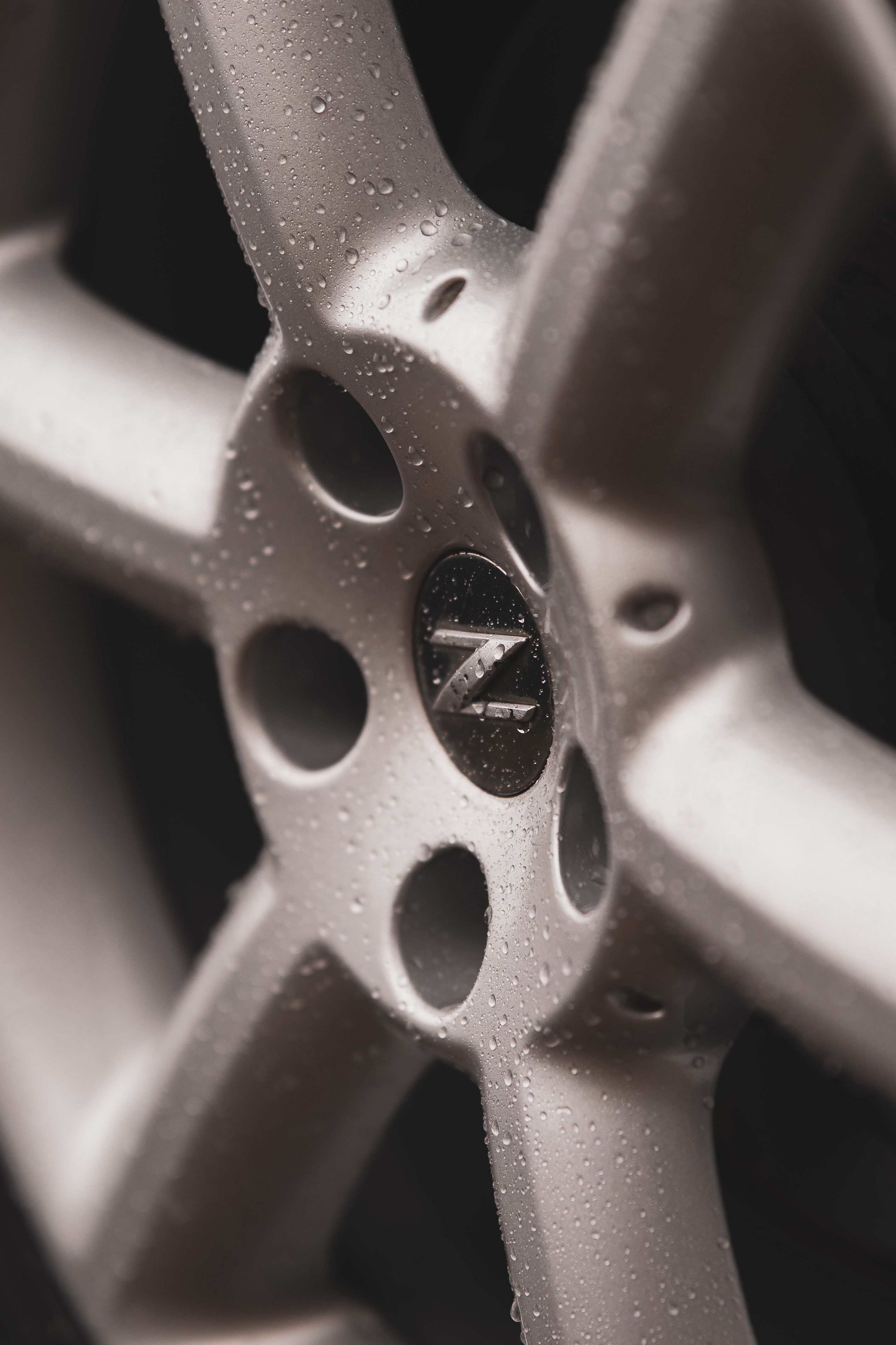 Detailed view of a sports car wheel featuring water droplets and chrome finishes.