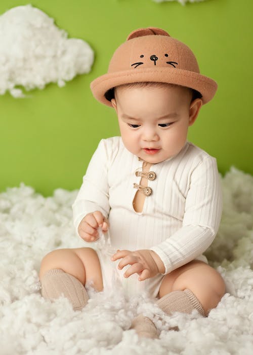 Adorable Asian baby sitting in soft fluffy clouds in studio on green background