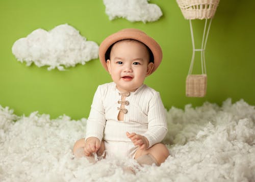 Cheerful ethnic baby sitting in clouds in studio