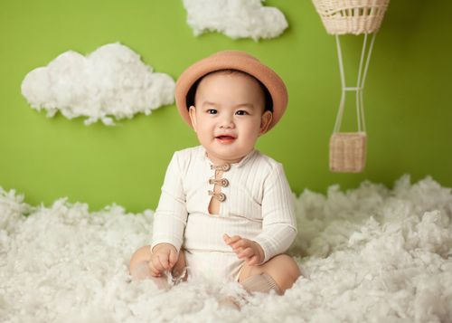 Free Smiling Asian baby sitting in soft comfortable cloud in studio on green background and looking away Stock Photo