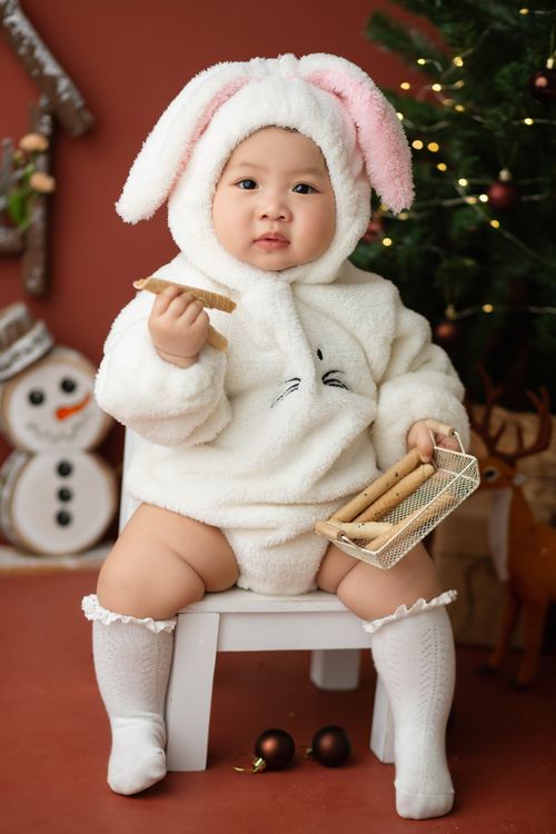 Free Sweet Asian little child in fluffy bunny costume sitting on stool in studio with Christmas decorations and looking at camera Stock Photo