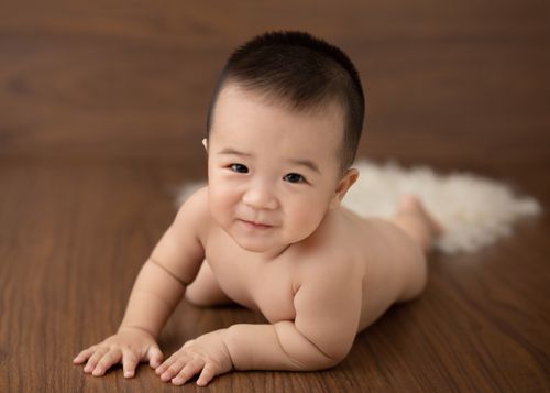 Free Delighted Asian little naked child lying on wooden floor in studio and looking at camera Stock Photo