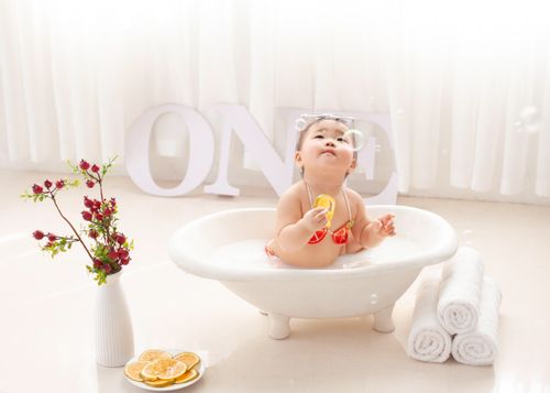 Free Cute Asian toddler in swimwear sitting in foamy water in bathtub and playing with soap bubbles Stock Photo