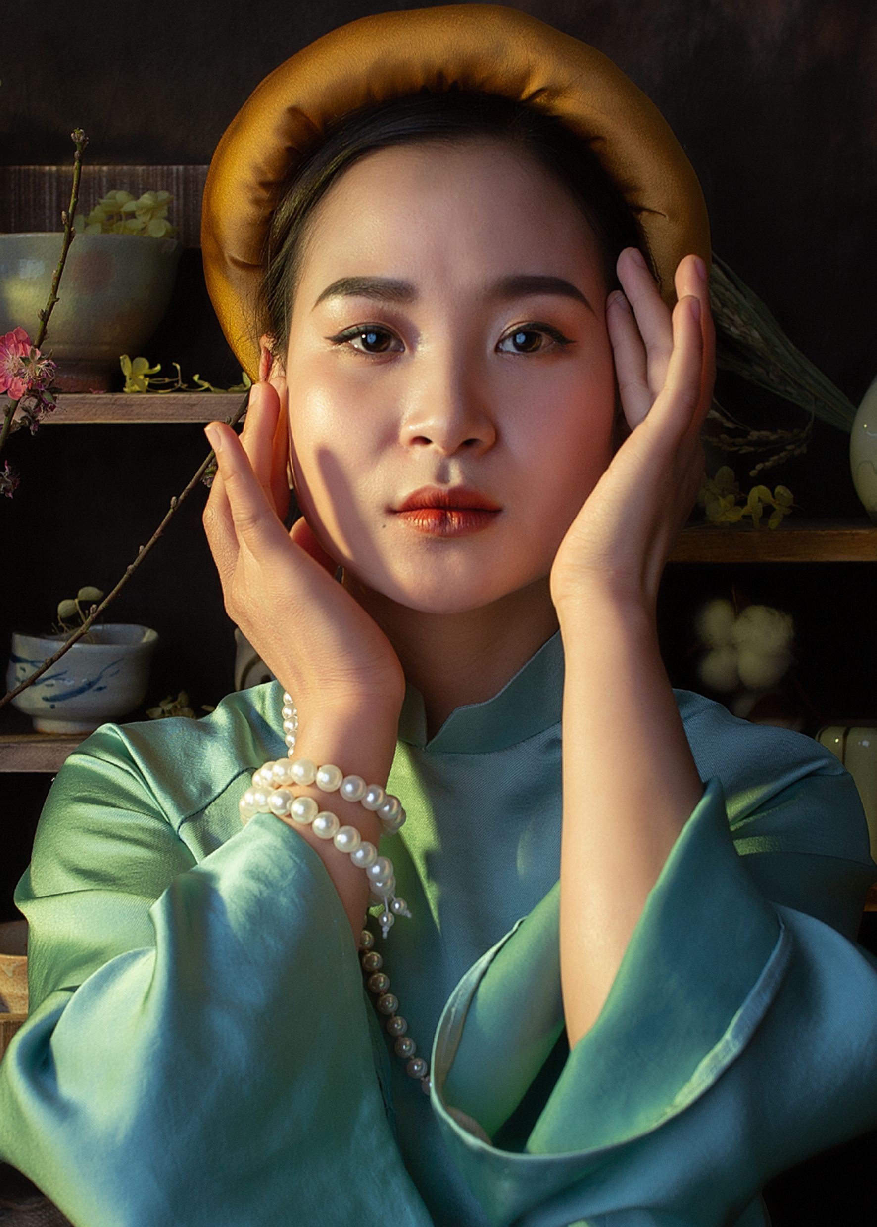 Tranquil charming Asian female in silk clothes and in trendy accessories touching face and looking at camera