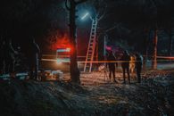 Group of colleagues investigating crime scene fenced with tape among trees at dark night