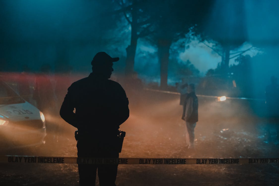 Free Silhouette of policeman and investigators standing behind crime scene boundary tape at night in forest Stock Photo