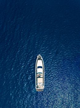 High-angle drone shot capturing a luxurious yacht floating in vibrant blue ocean waters.