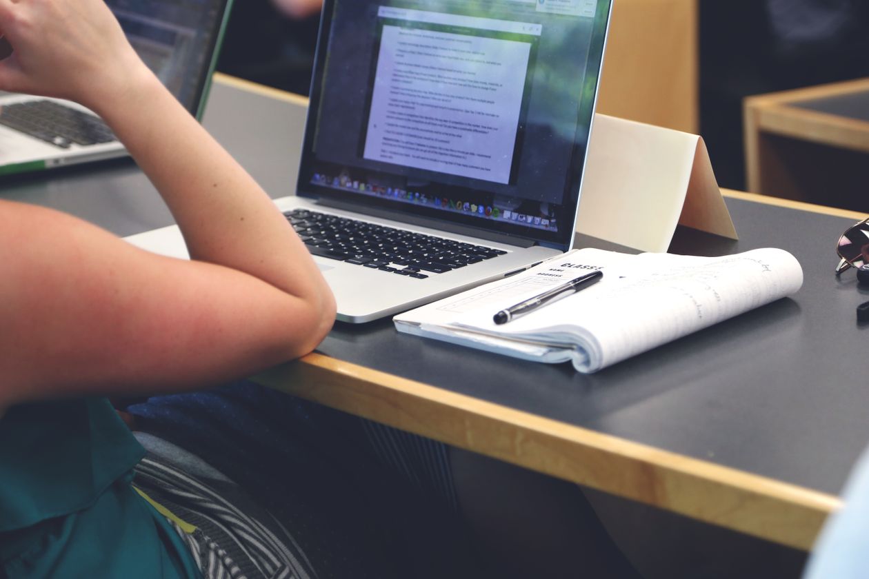 A student taking notes beside an open laptop in a classroom