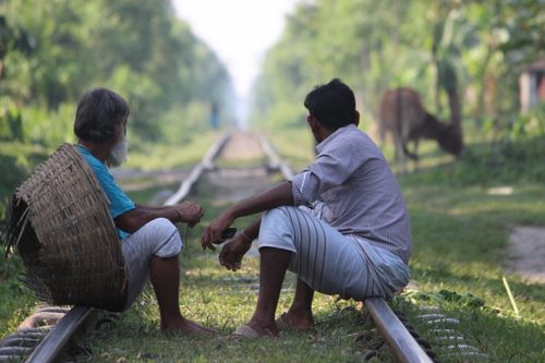 Free Two men sitting on railway track in rural Bangladesh, showcasing countryside life. Stock Photo