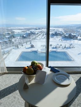 Sunlit winter landscape at a resort with pool, snow, and fruit on a table.