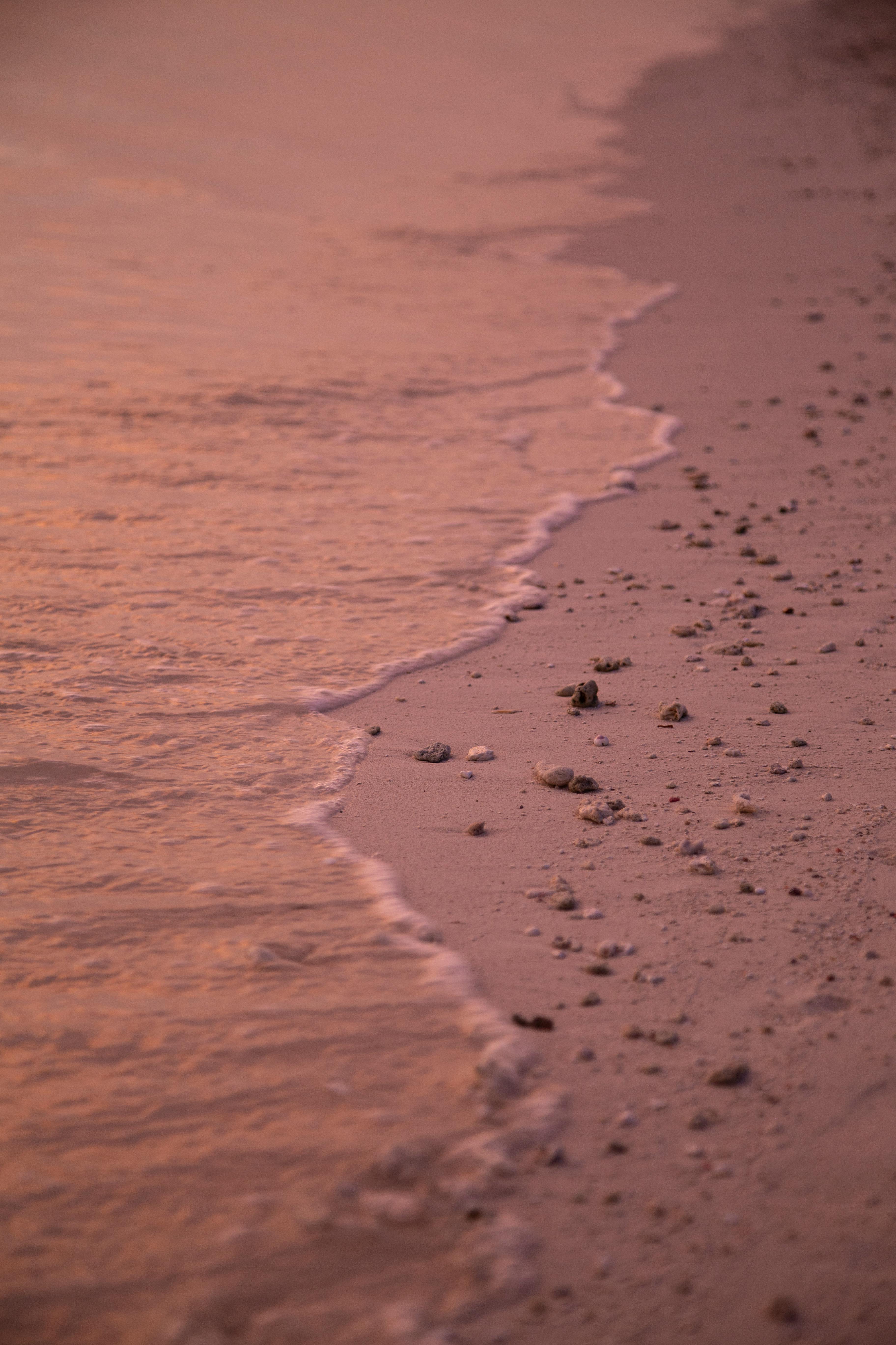 Calm waves gently lap against the soft sandy beach of Thoddoo, Maldives at sunset, creating a serene and picturesque scene.