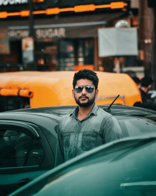 Free A fashionable man in sunglasses stands among cars in a bustling city scene. Stock Photo