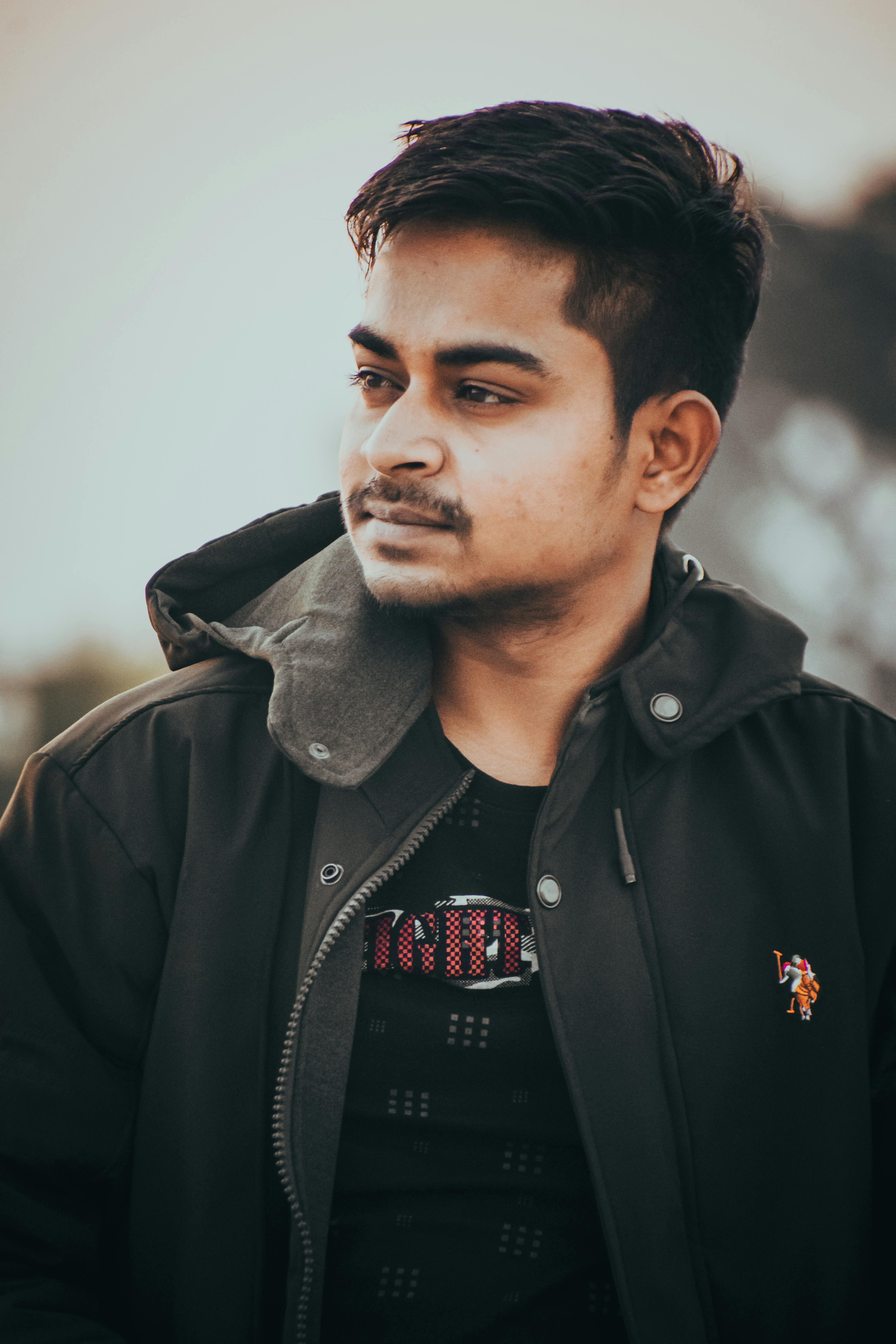 Portrait of a young man wearing a green jacket in an outdoor setting with a blurred background.