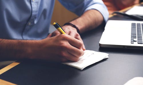 Person Writing on Paper Using Yellow and Black Pen