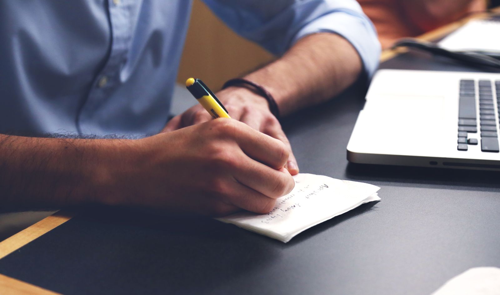 Close-up of someone writing notes with a pen next to an open laptop.