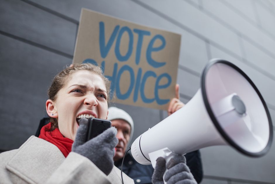 Woman passionately speaking through a megaphone during a winter protest with a visible vote choice sign.