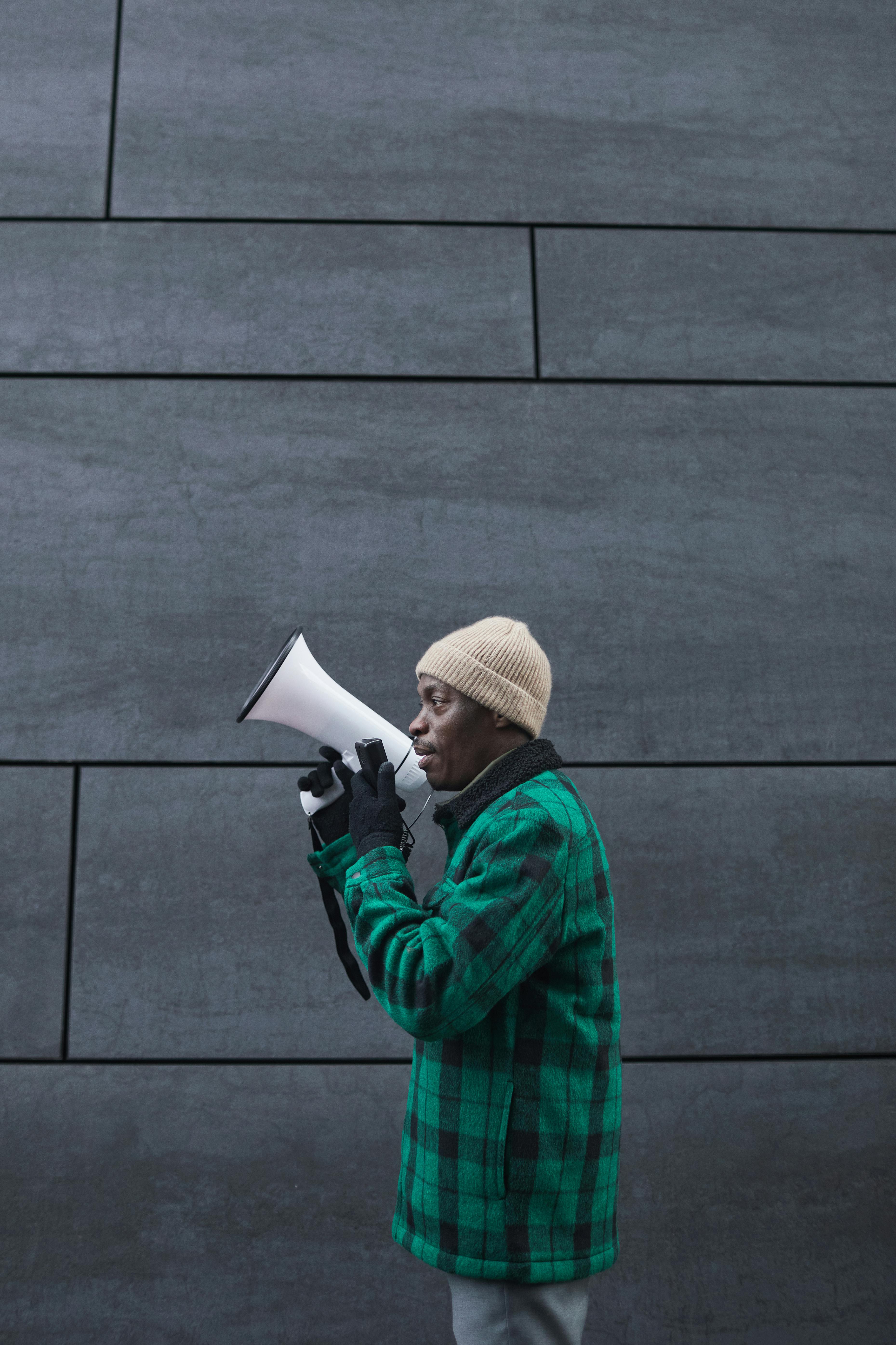 An adult man with a megaphone against a dark wall background, emphasizing communication.