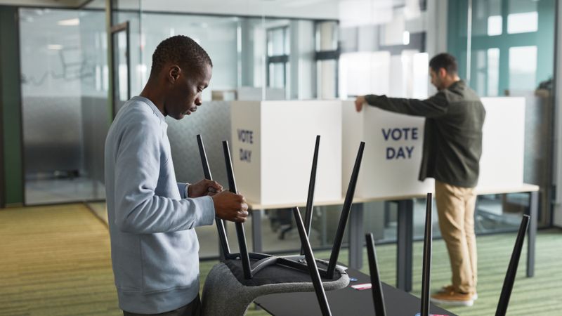 Men preparing voting booths indoors for election day, enhancing democracy.