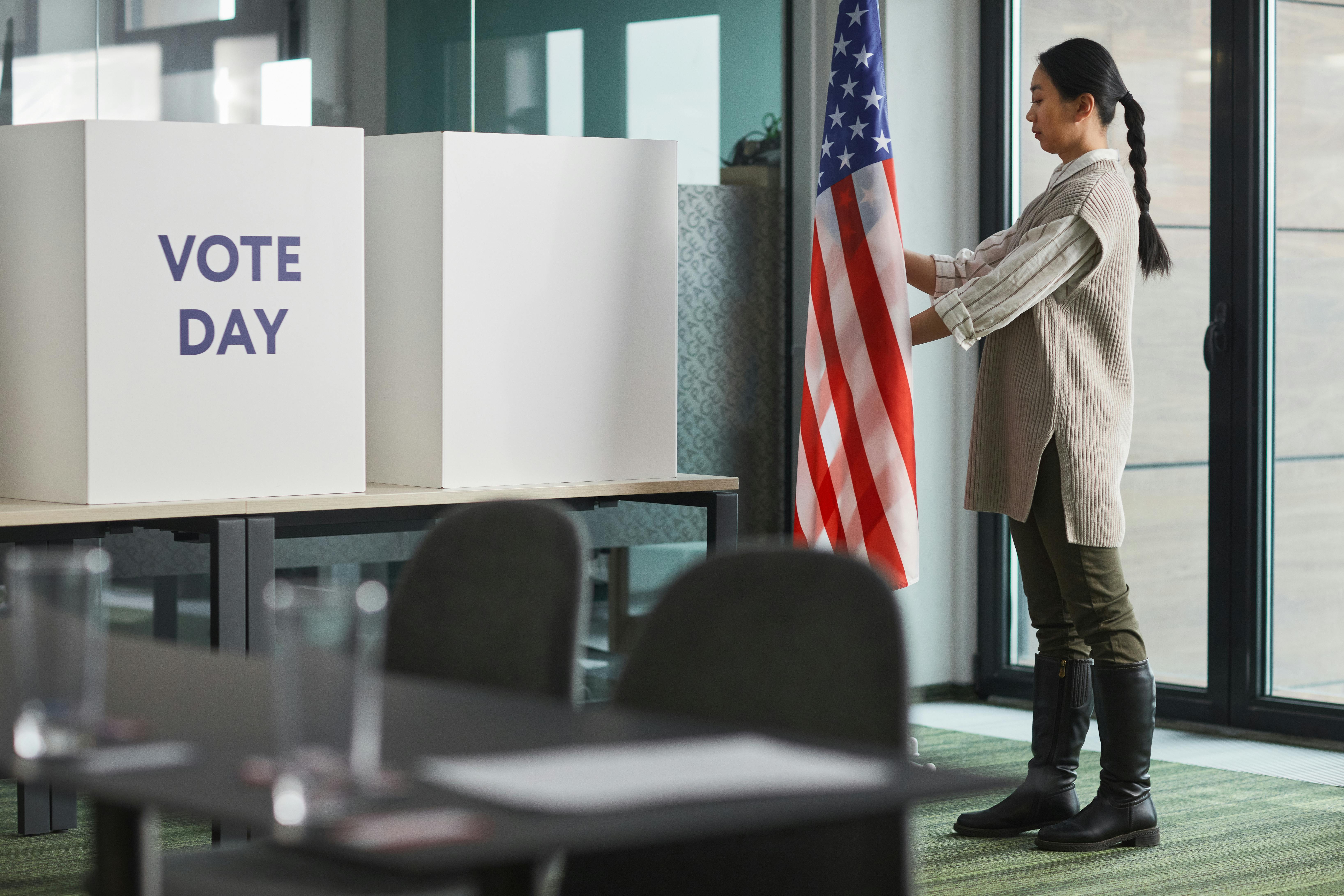 Woman standing near American flag and ballot boxes during voting day