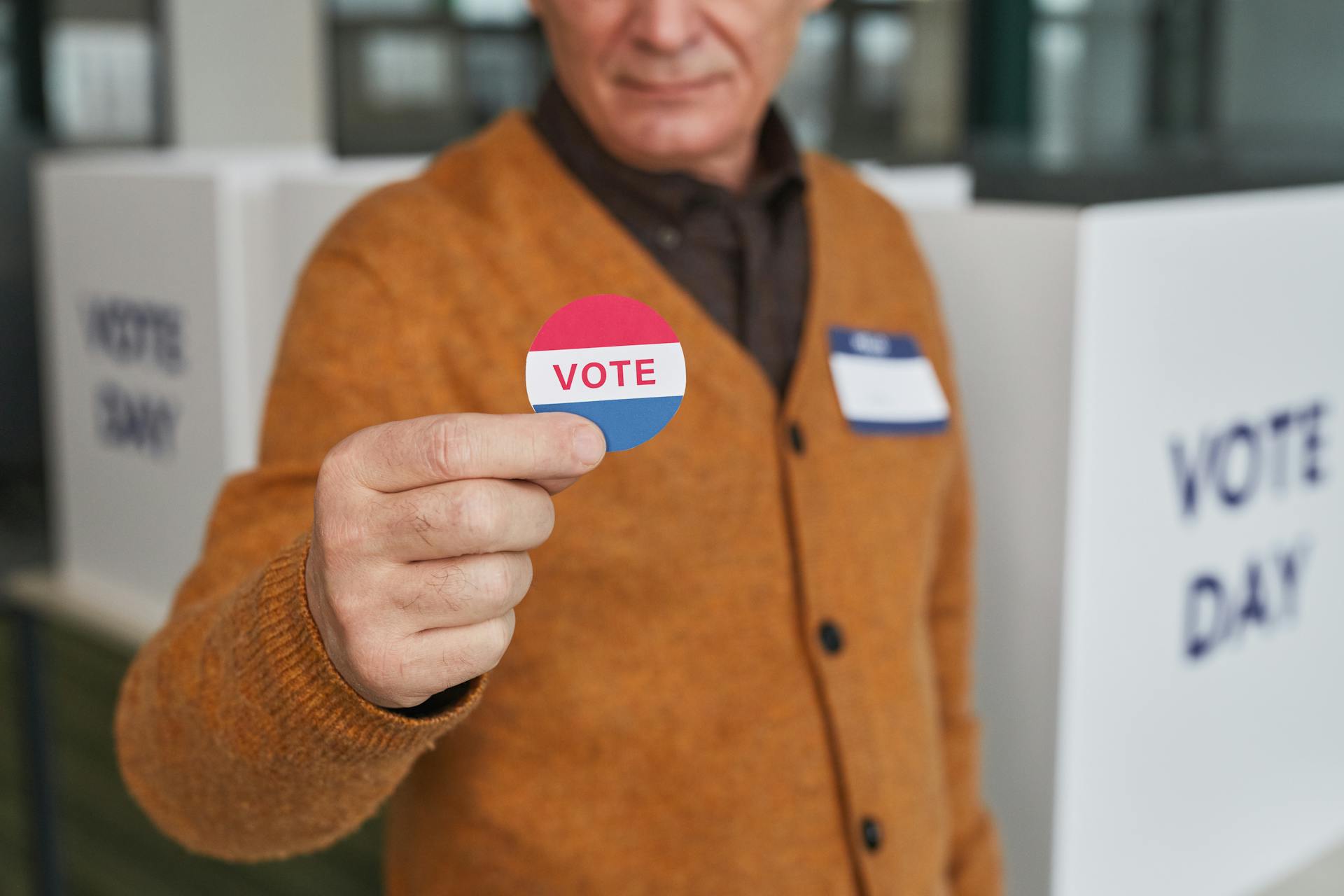 A senior adult holding a vote sticker inside a polling booth during election day.