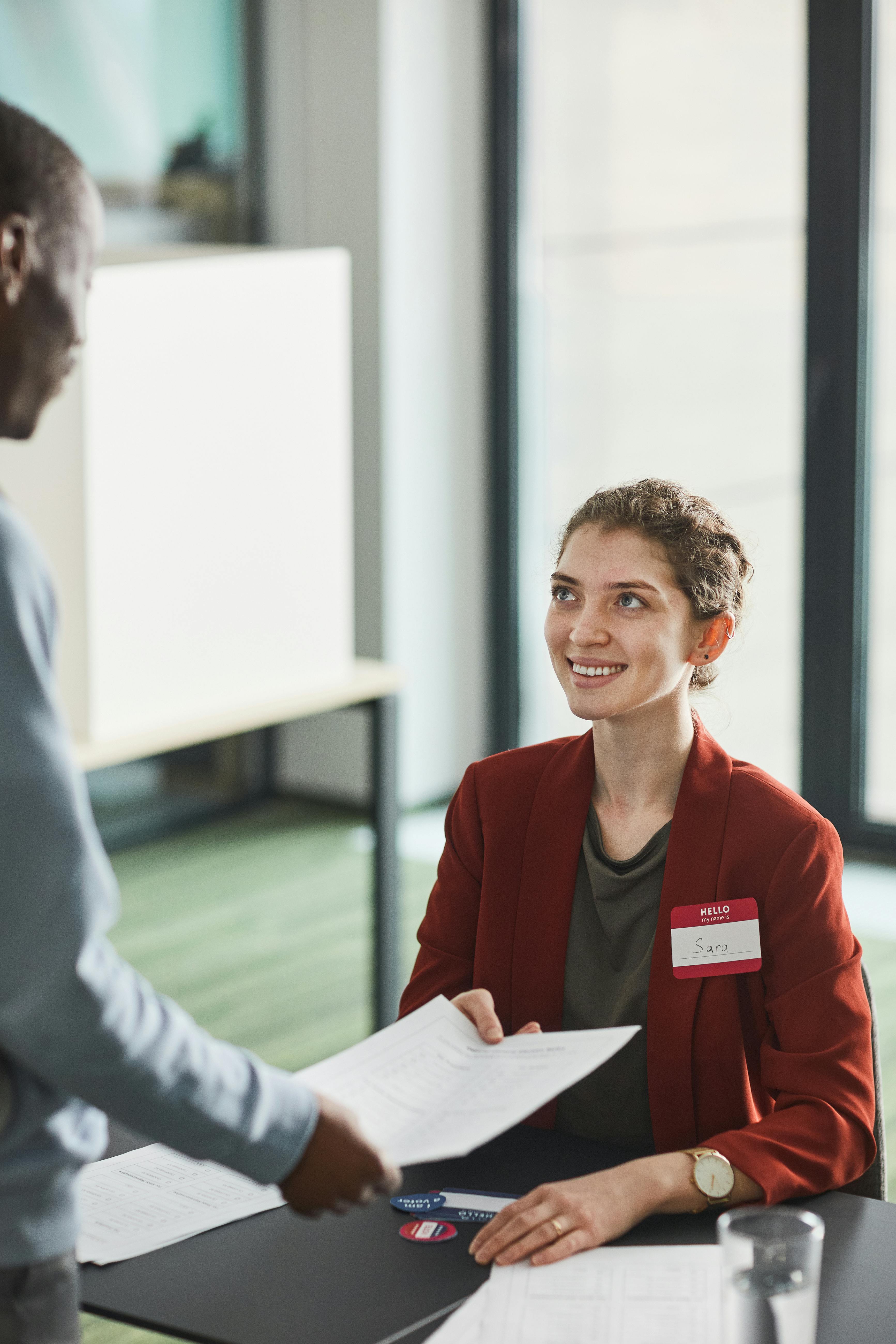 woman in orange blazer smiling handing a month a document