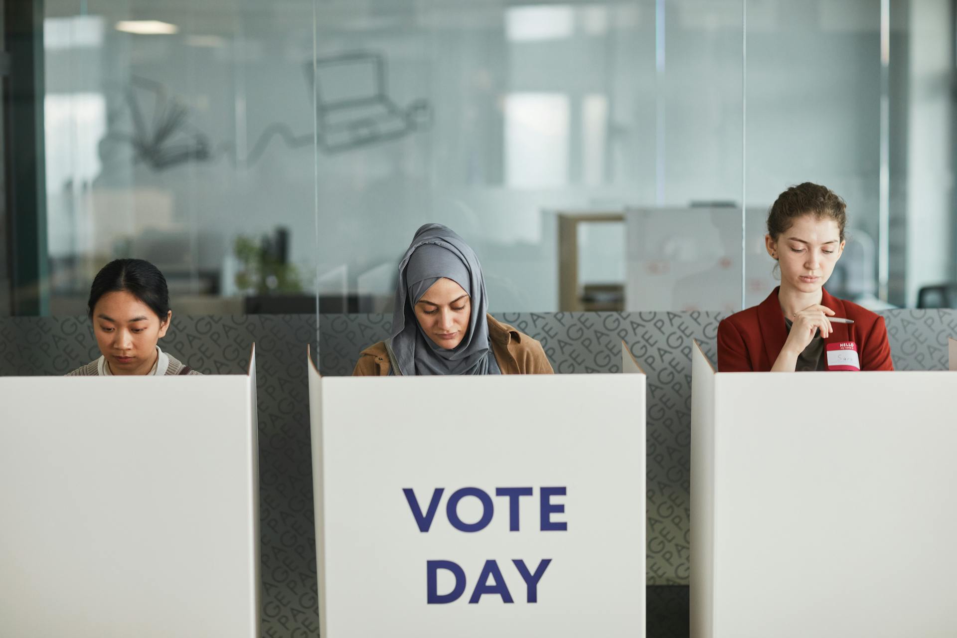 Three women voting in office cubicles. Diverse representation, focused and serious.