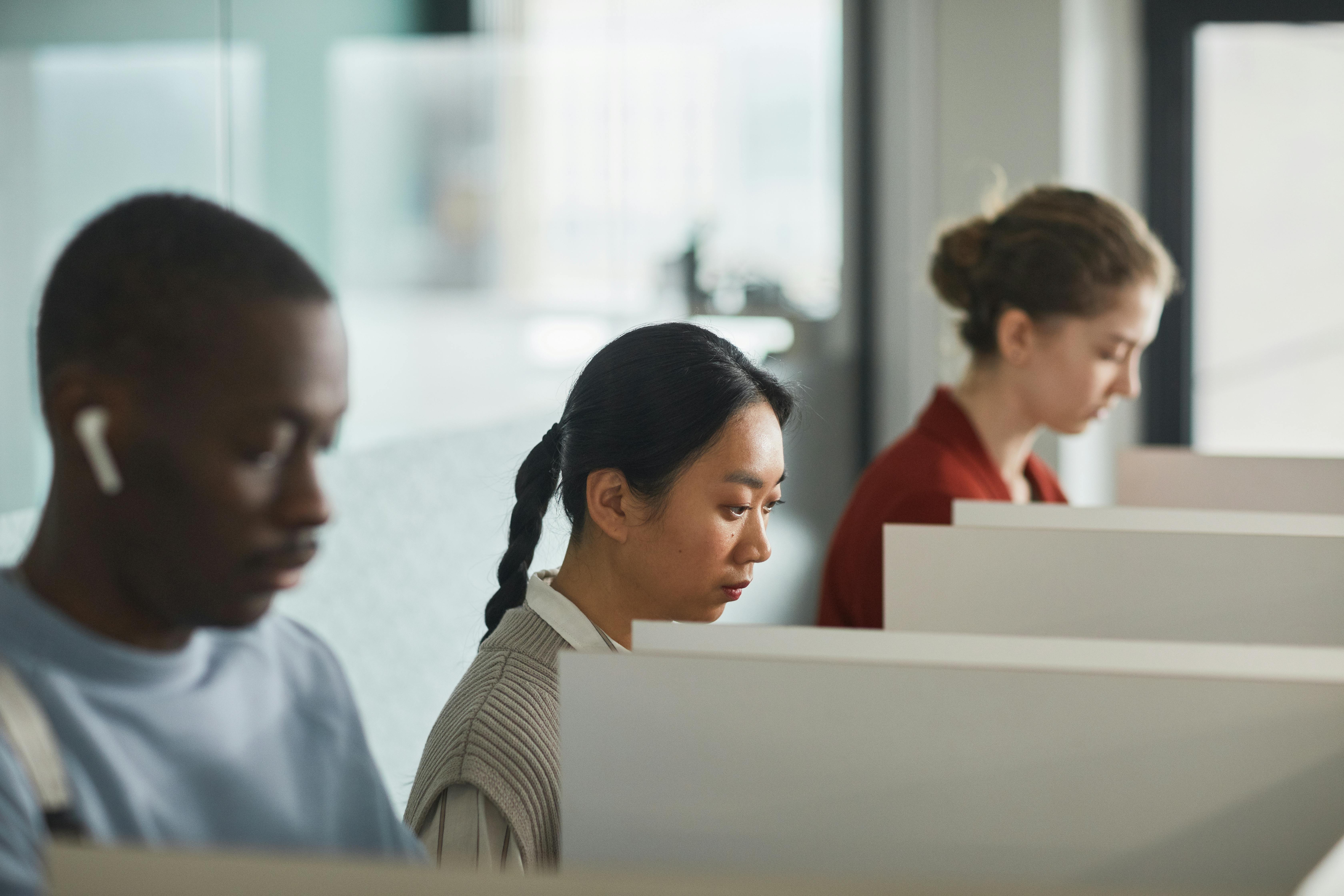 Employees working in cubicles using technology, showcasing a diverse and focused office environment.