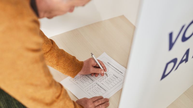 Senior man marking a ballot at a voting booth in an indoor polling station.