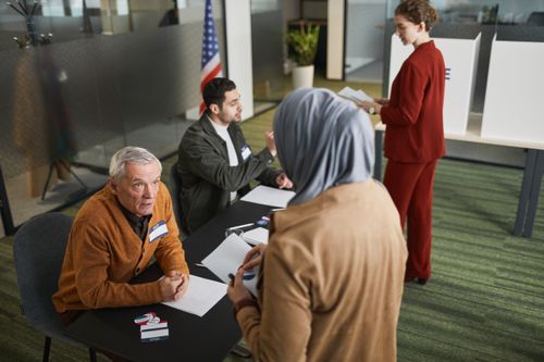 Free Adults engaging in the voting process at an indoor polling station, representing diverse backgrounds and social responsibility. Stock Photo