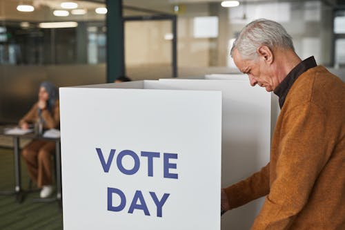 Man in Brown Sweater Standing by the Polling Place